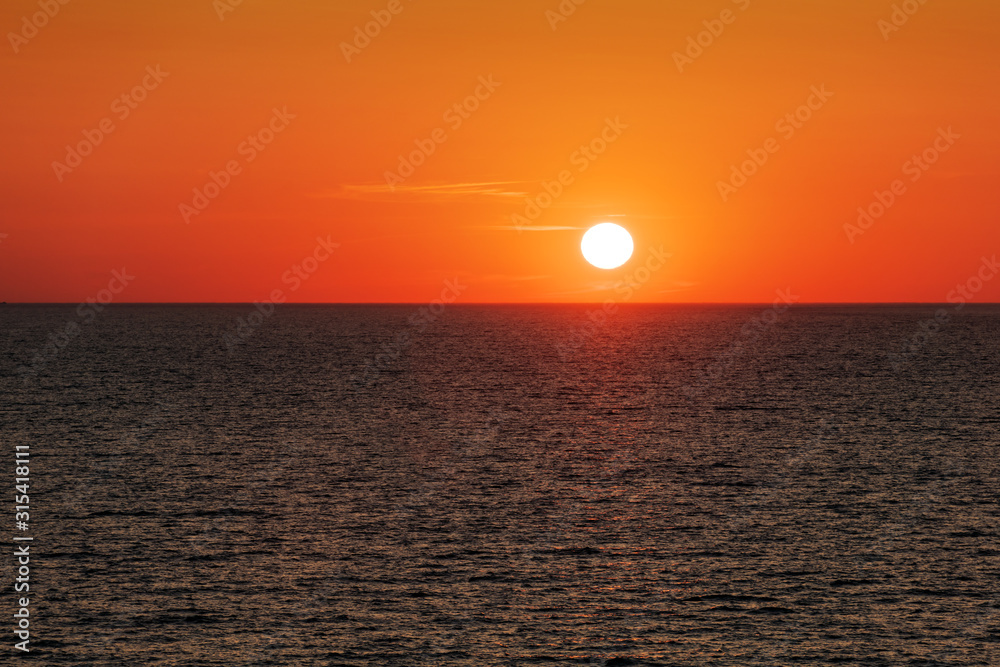 Sunset in the ocean with large sun dusk soft waves and red cloudy sky. Sea sunrise background. Landscape photography