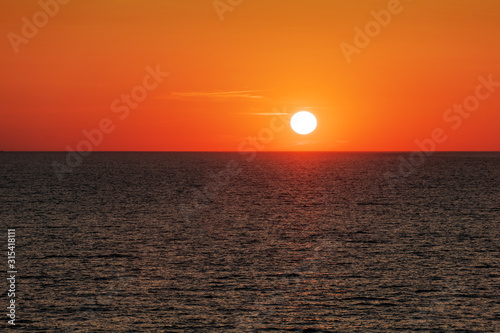Sunset in the ocean with large sun dusk soft waves and red cloudy sky. Sea sunrise background. Landscape photography