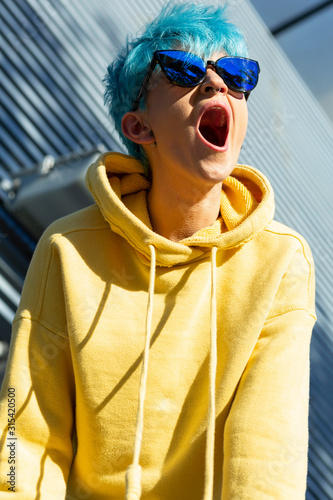 Portrait of screming young woman with dyed blue hair wearing yellow hooded jacket photo