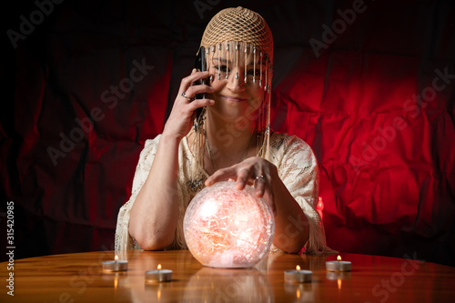 Fortune Teller with Crystal Ball and mobile phone on table with candles. Smartphone, online or call concept
