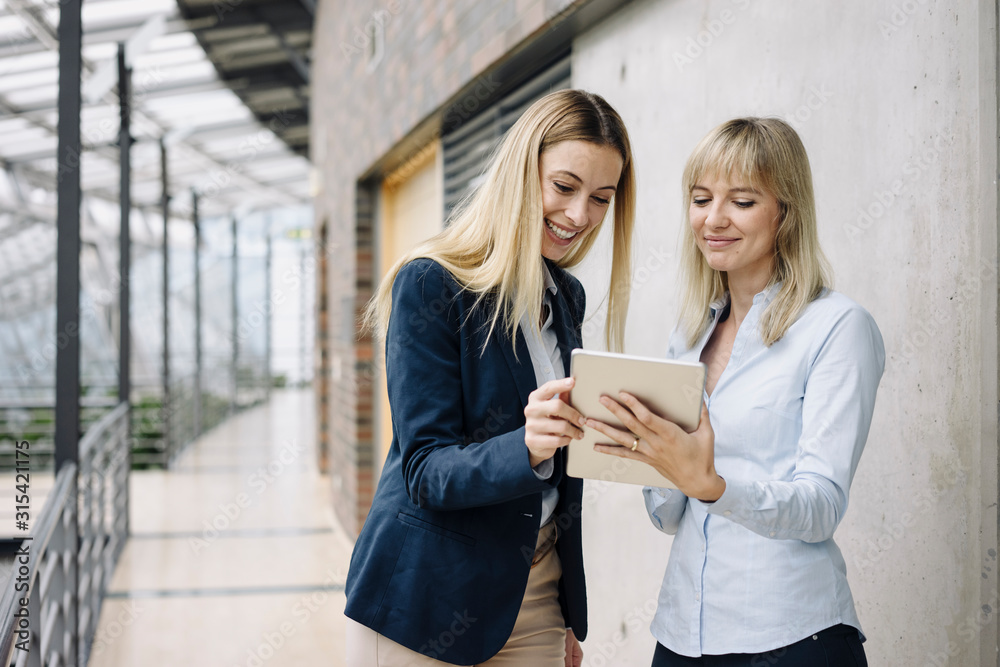 Two happy young businesswomen with tablet in modern office building Two happy young businesswomen with tablet in modern office building