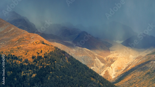 The landscape is raining and the bright sun shines in the mountains in autumn. 