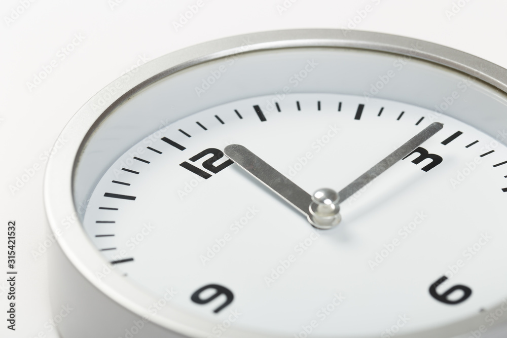 15 minutes after twelve white with light metal minimalistic clock close-up on a light background 15 minutes after twelve white with light metal minimalistic clock close-up on a light background