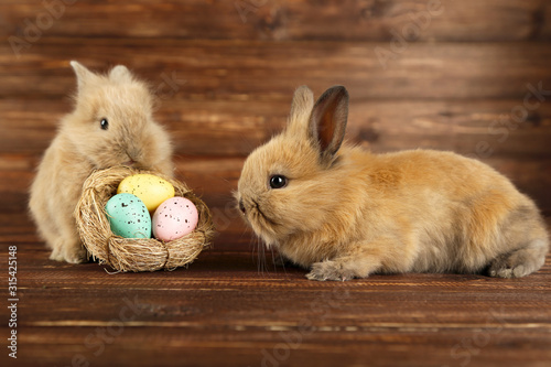 Bunny rabbits with easter eggs in basket on brown wooden background