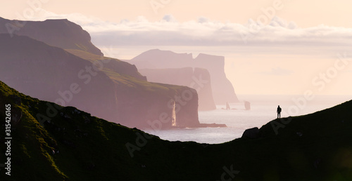 Fotografia, Obraz Man silhouette on background of famous Risin og Kellingin rocks and cliffs of Eysturoy and Streymoy Islands seen from Kalsoy Island