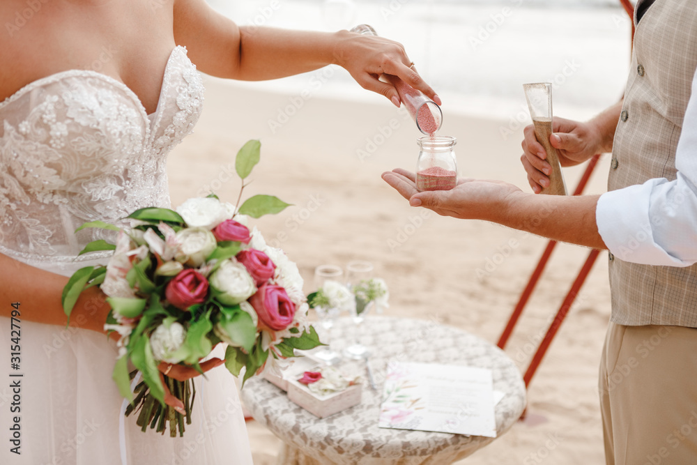 Stylish happy couple on the luxury outdoor wedding ceremony, hands of newlyweds close up. Sand ceremony Stylish happy couple on the luxury outdoor wedding ceremony, hands of newlyweds close up. Sand ceremony