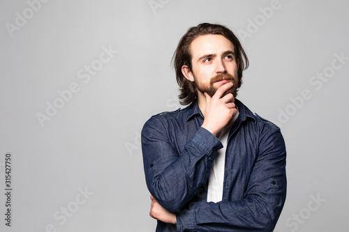Fotomural Young calm guy in glasses dreaming and touching chin isolated on gray background