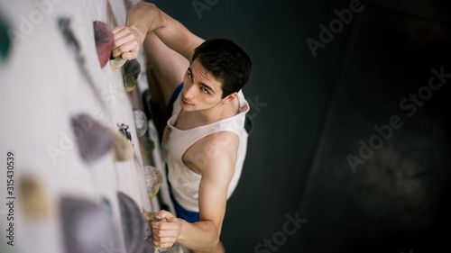 athletischer Mann beim Bouldern an Kletterwand sieht nach oben photo