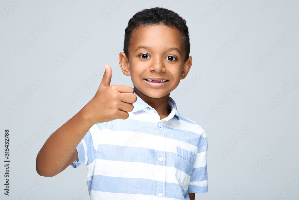 Young African American boy showing thumb up on grey background Young African American boy showing thumb up on grey background
