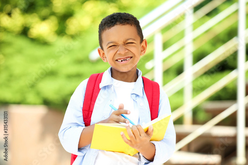 Young African American school boy writing in notepad with backpack and on the street