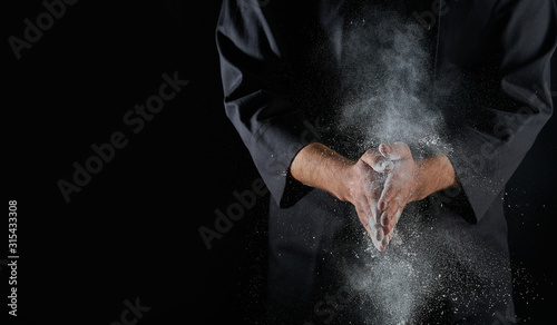 Male hands and splash of white wheat flour on a black background