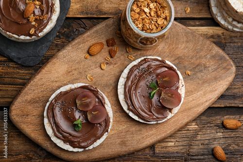 Puffed rice cakes with chocolate spread and grape on wooden table, flat lay