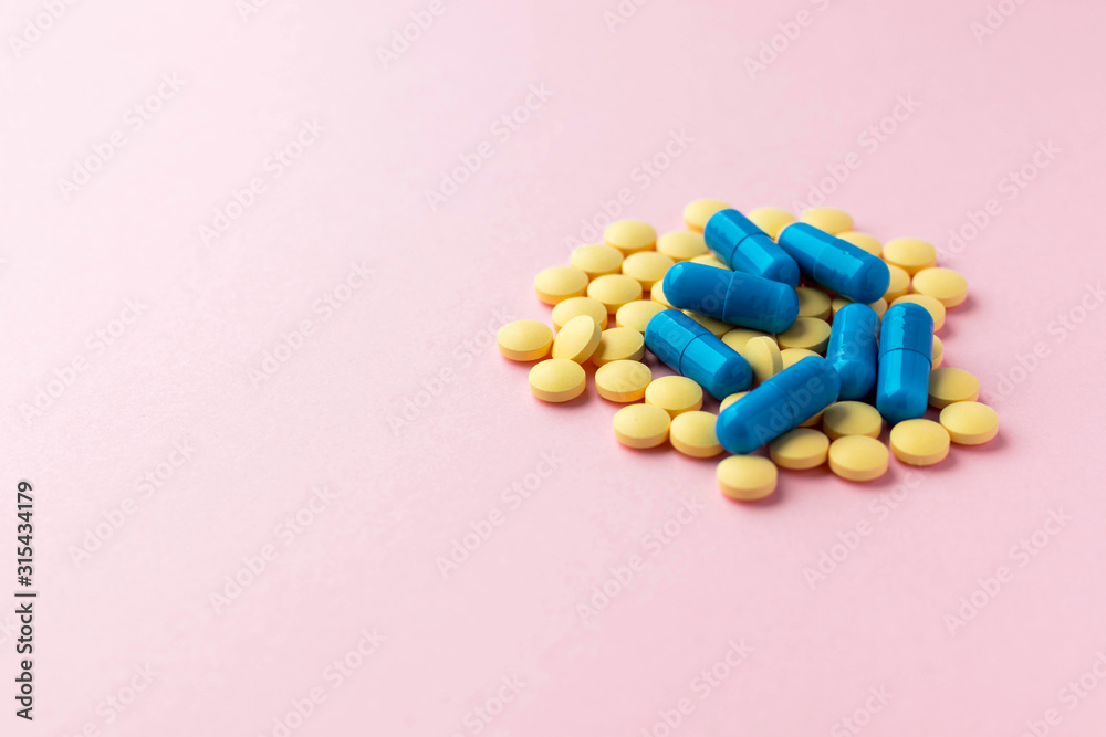 Heap of round yellow pills and blue capsules on light pink background. Prescription drugs. Woman health. Epidemic, painkillers, healthcare and treatment concept. Copy space. Heap of round yellow pills and blue capsules on light pink background. Prescription drugs. Woman health. Epidemic, painkillers, healthcare and treatment concept. Copy space.