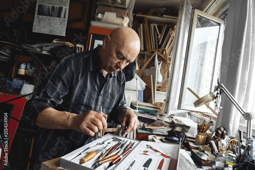 Man working at typograhpy studio indoors choosing tool pensive
