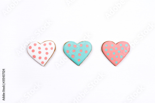 Three gingerbread cookies with frosting in the shape of a heart on white wooden background. Valentines day concept. Flat lay, top view.