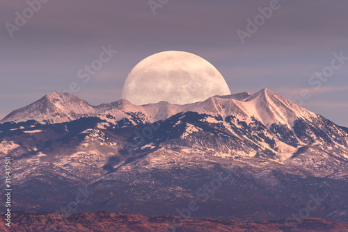 Full moon at it's perigee rising behind La Sal Mountains in Canyonlands National Park during sunset