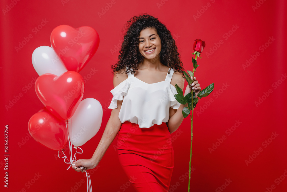 black woman smiling with heart shaped balloons and rose isolated on red background black woman smiling with heart shaped balloons and rose isolated on red background