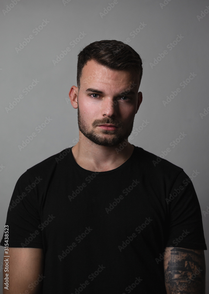  Portrait of young and fit fashion model with tattoos on grey background. Portrait of pretty young guy with short hair - rembrandt lighting. Shot of man with grey tones