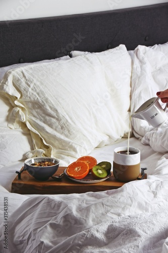 Hygge healthy breakfast in bed. Food tray with coffee and fruits on the white bed linen background