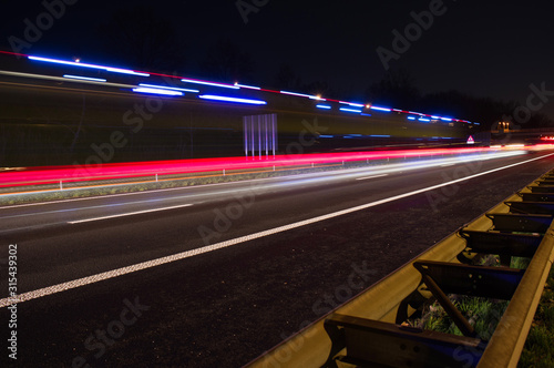 Highway at night with traffic and blue siren blurred by motion with guardrail in the foreground in Arnhem, Netherlands