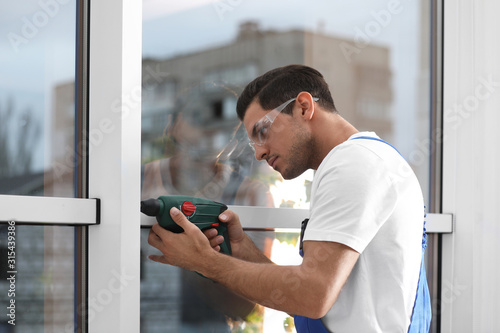 Construction worker repairing plastic window with electric screwdriver indoors
