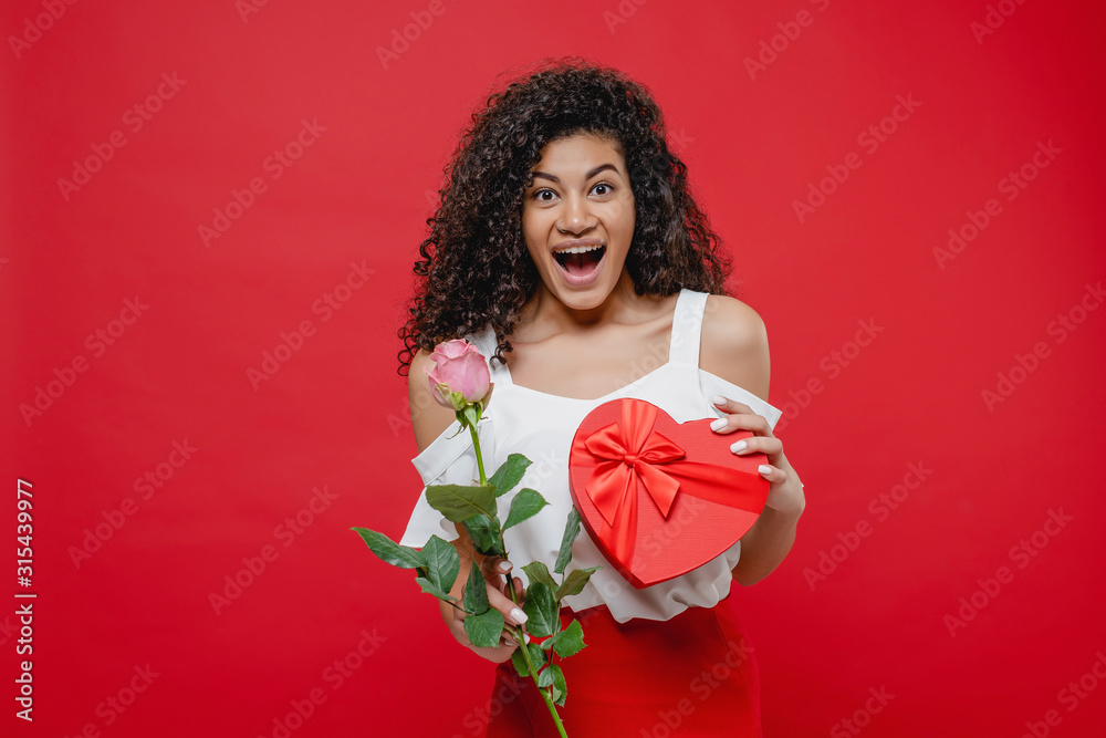 happy screaming black woman with pink rose and heart shaped valentine gift isolated over red happy screaming black woman with pink rose and heart shaped valentine gift isolated over red