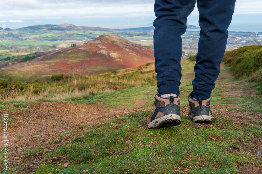 Closeup of young hiker legs wearing hiking boots, walking in a blurred Irish mountain winter landscape. Outdoor fitness, activity and sports, healthy lifestyle concept. Closeup of young hiker legs wearing hiking boots, walking in a blurred Irish mountain winter landscape. Outdoor fitness, activity and sports, healthy lifestyle concept.