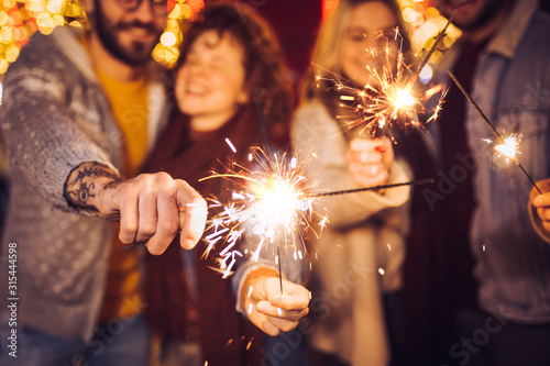 Close view of sparklers. Group of happy friends celebrating New Year with sparklers. New year party.