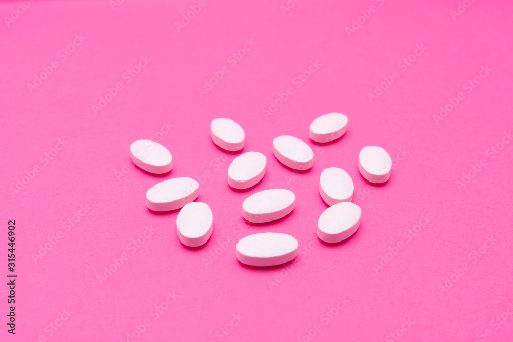 White oval pills lie on a pink background. Copy space, macro White oval pills lie on a pink background. Copy space, macro