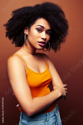 pretty young african american woman with curly hair posing cheerful gesturing on brown background, lifestyle people concept