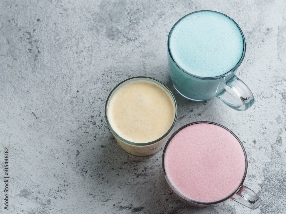 Trendy drinks: Blue, yellow and pink latte. Top view of hot butterfly pea or blue spirulina latte, yellow or gold turmeric latte and pink beetroot latte on gray cement background. Copy space for text Trendy drinks: Blue, yellow and pink latte. Top view of hot butterfly pea or blue spirulina latte, yellow or gold turmeric latte and pink beetroot latte on gray cement background. Copy space for text