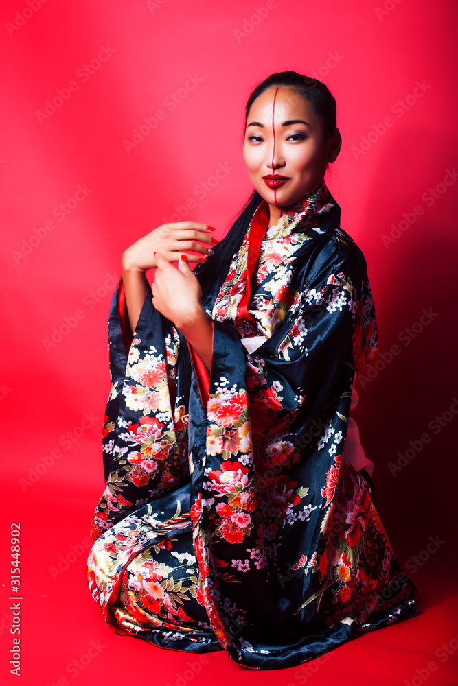 young pretty geisha on red background posing in kimono, oriental concept