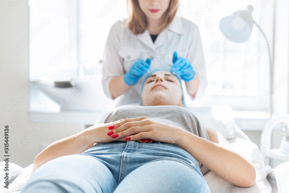Woman professional doctor beautician applies a mask on a patient's face for skin care. Cosmetic procedures for skin rejuvenation and nutrition
