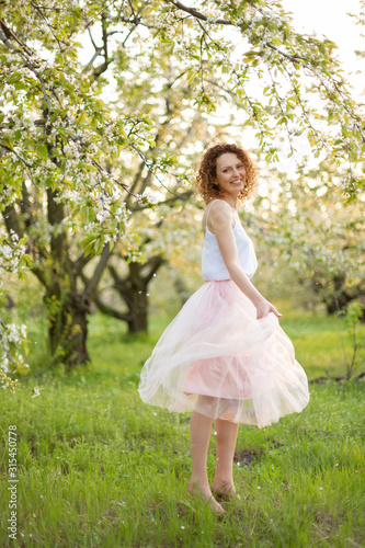 Young attractive woman with curly hair walking in a green flowered garden. Spring romantic mood