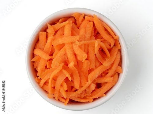 Fresh organic shredded carrots in small white bowl. Raw grated carrots isolated on white with clipping path. Top view or flat lay.