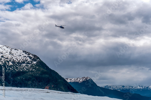 Blue helicopter is flying over the glacier in Alaska. Expedition with excursion group. Amazing views of the snow peaks. 