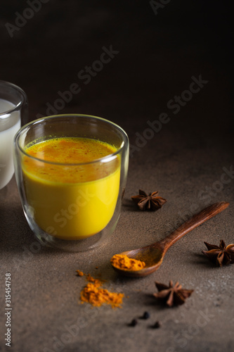Golden milk with turmeric powder in glass over dark grunge background, copy space. Health and energy boosting, flu remedy, natural cold fighting drink. Clean eating, detox, weight loss concept