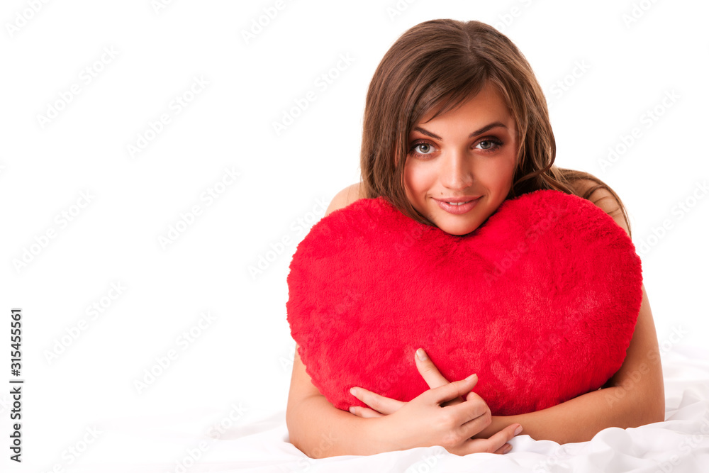 Young beautiful brunette woman in beige dress sitting and holding big red toy heart in hands over white background Young beautiful brunette woman in beige dress sitting and holding big red toy heart in hands over white background