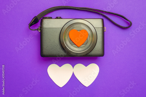 St. Valentine's Day. A camera and two white hearts for photography on a lilac background. View from above.