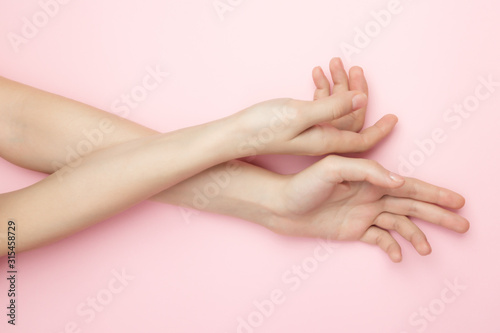 The woman hands on a pink background. Cosmetics for a sensitive skin care. Natural petal cosmetics, anti-wrinkle hand care. A thin wrist and natural manicure. photo