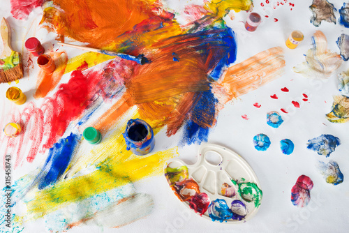 Bright multi-colored childrens drawings with paints, brushes and palette stained with paint
