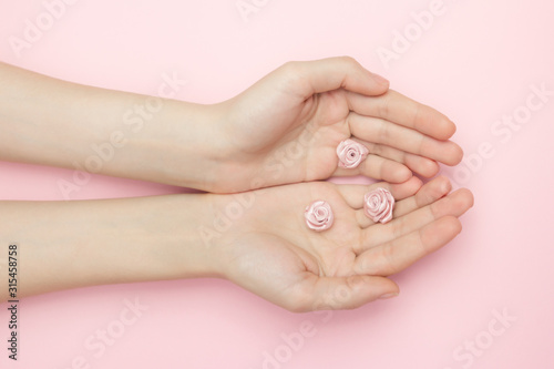 The woman hands hold rose flowers on a pink background. A thin wrist and natural manicure. Cosmetics for a sensitive skin care. Natural petal cosmetics  anti-wrinkle hand care.