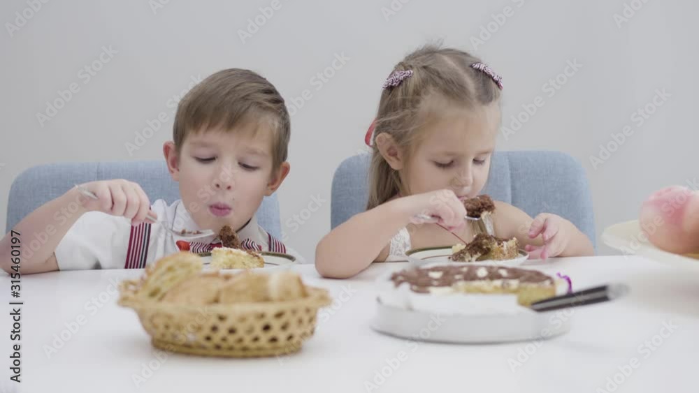 Close-up faces of cute Caucasian boy and girl eating cake. Little brother and sister enjoying sweet food at birthday party. Happiness, leisure. Close-up faces of cute Caucasian boy and girl eating cake. Little brother and sister enjoying sweet food at birthday party. Happiness, leisure.