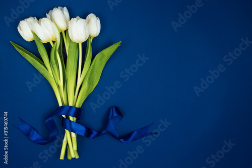 A bouquet of white tulips tied with a ribbon. On a blue background. Postcard for Valentine's Day and March 8th #315460744