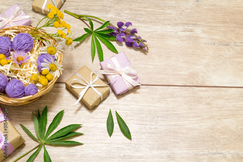 Presents in violet and kraft paper on the wooden table. Purple, white and yellow flowers lay around.
