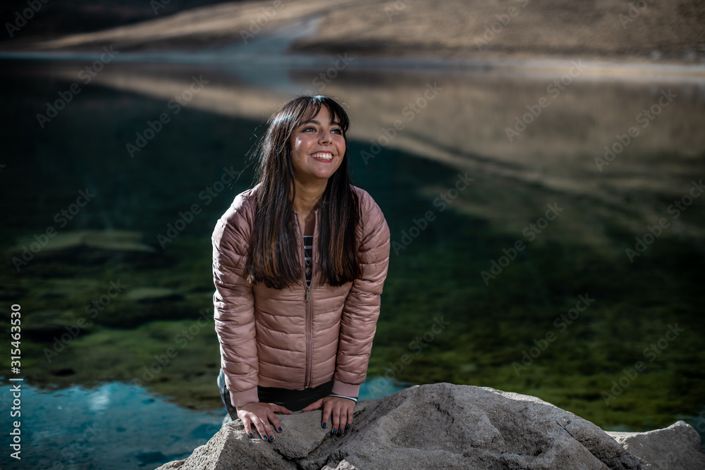 Girl smiling on a rock, wearing a pink jacket, in winter beside the lake in the mountains, in the Snowy Toluca. Girl smiling on a rock, wearing a pink jacket, in winter beside the lake in the mountains, in the Snowy Toluca.