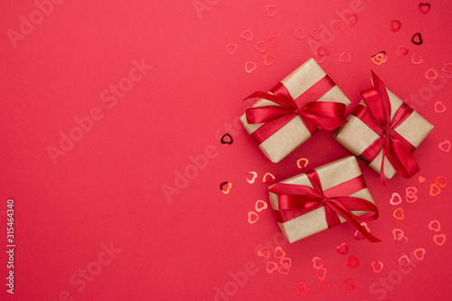 Gift boxes wrapped with kraft paper and red bow isolated on red background. Abstract flat lay.