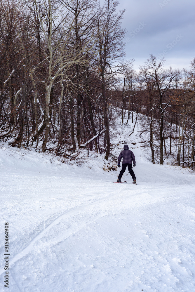 A man on a cloudy winter day is skiing down the mountainside.