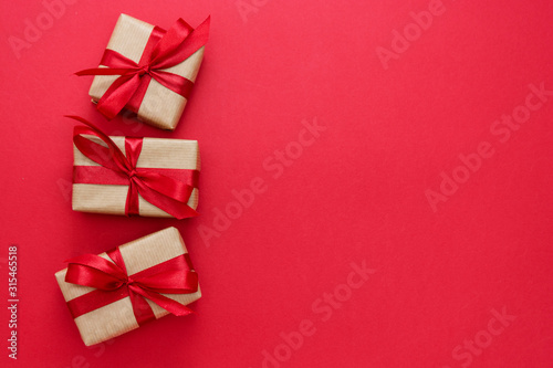 Gift boxes wrapped with kraft paper and red bow isolated on red background. Abstract flat lay.