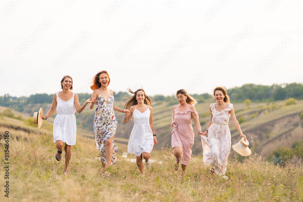The company of cheerful female friends have a great time together on a picnic in a picturesque place overlooking the green hills. Girls in white dresses dancing in the field The company of cheerful female friends have a great time together on a picnic in a picturesque place overlooking the green hills. Girls in white dresses dancing in the field
